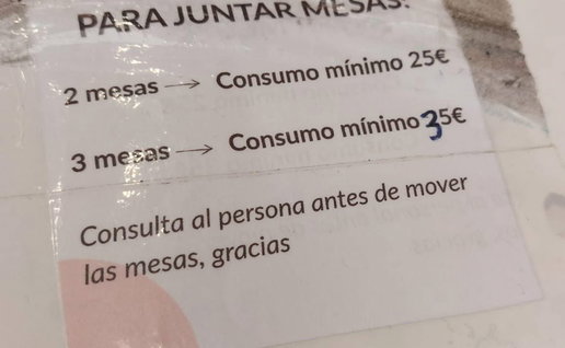 Sign at a Spain café terrace stating customers must meet a minimum spend to join tables together