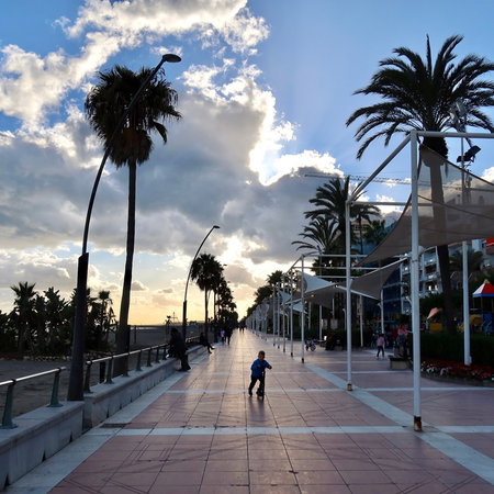 Palm lined promenade in Spain under mixed sunshine and dark clouds before May holiday weekend
