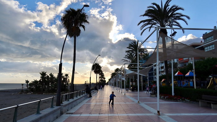 Palm lined promenade in Spain under mixed sunshine and dark clouds before May holiday weekend