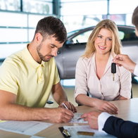 young couple buying a car on finance signing paperwork