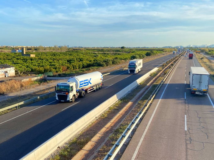 A fuel tanker and freight trucks driving on a multi-lane motorway in Spain, illustrating the impact of new transport price laws and fuel cost adjustments.
