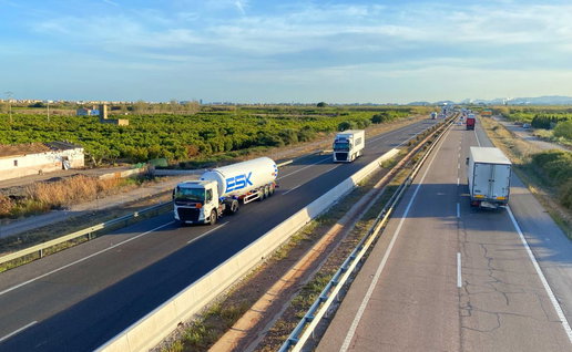 A fuel tanker and freight trucks driving on a multi-lane motorway in Spain, illustrating the impact of new transport price laws and fuel cost adjustments.