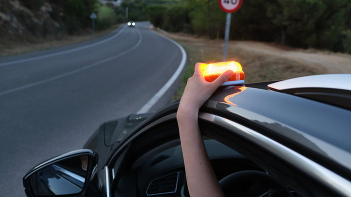 Driver placing V16 emergency beacon on car roof during roadside stop in Spain