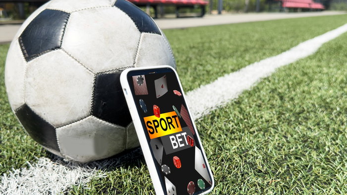 Live in-play betting app on a mobile phone screen on a football pitch with a football