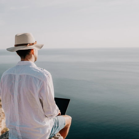 Remote worker using a laptop while sitting by the sea in a sunny location
