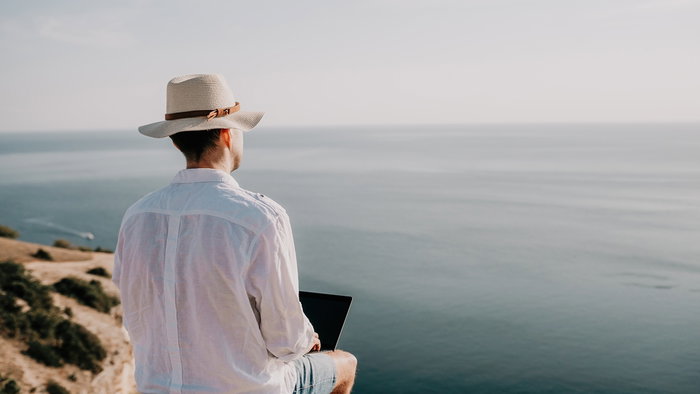 Remote worker using a laptop while sitting by the sea in a sunny location