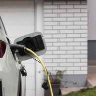 Electric car charging at home outside a modern house with charging cable plugged into the vehicle.