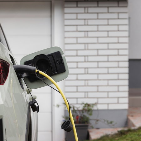 Electric car charging at home outside a modern house with charging cable plugged into the vehicle.