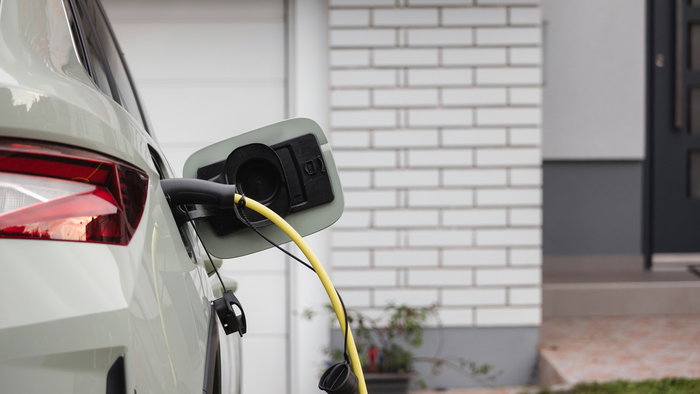 Electric car charging at home outside a modern house with charging cable plugged into the vehicle.