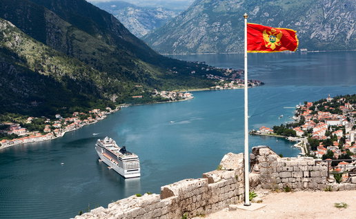 Montenegro flag overlooking Kotor Bay with cruise ship and coastal mountains in Montenegro
