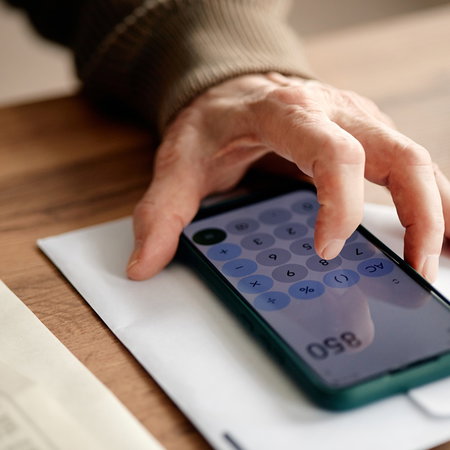 Person calculating pension-related payment on smartphone with documents on table
