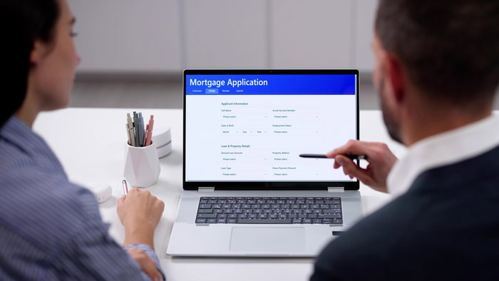 Person filling out mortgage application form with documents and calculator