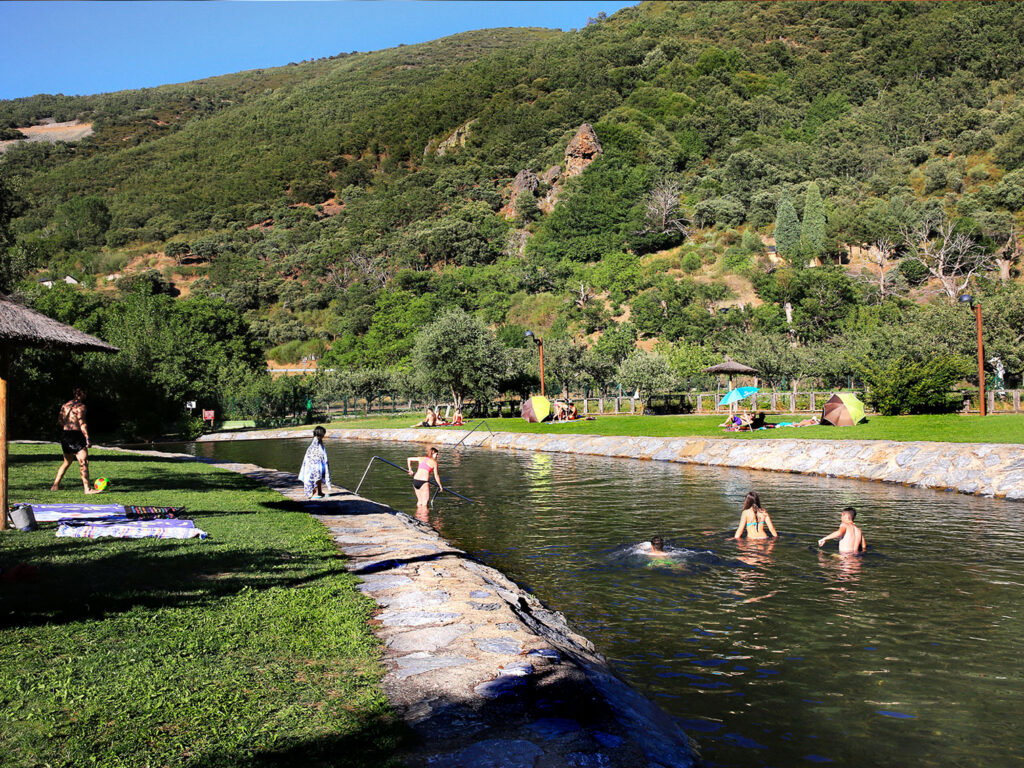 People swimming in a natural river pool in San Facundo, León, Spain, surrounded by green hills