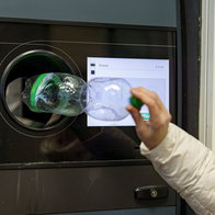 Woman placing a plastic bottle inside a recycling machine