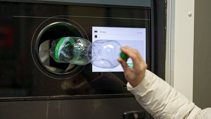 Woman placing a plastic bottle inside a recycling machine