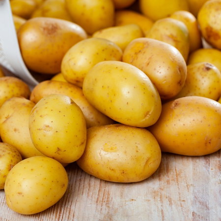 Freshly washed potatoes, poured out of a bucket on a wooden table. Ingredients for cooking.