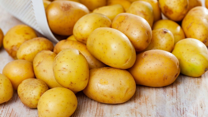 Freshly washed potatoes, poured out of a bucket on a wooden table. Ingredients for cooking.