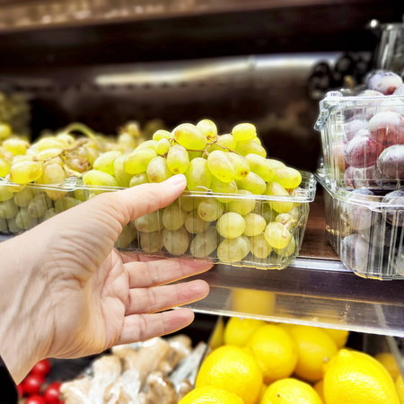 Hand taking grapes off a shelf in a supermarket