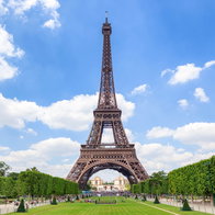 The Eiffel Tower stands tall and majestic against a vivid blue sky, framed by symmetrical green lawns and trimmed trees.
