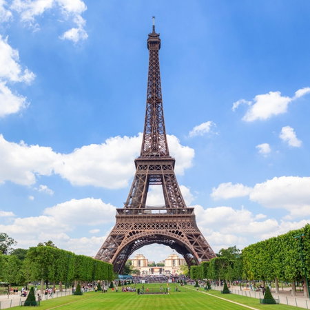 The Eiffel Tower stands tall and majestic against a vivid blue sky, framed by symmetrical green lawns and trimmed trees.