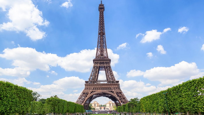 The Eiffel Tower stands tall and majestic against a vivid blue sky, framed by symmetrical green lawns and trimmed trees.