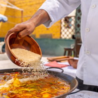 Chef adding rice to a delicious paella from a wooden bowl, cooking outdoors for a family lunch