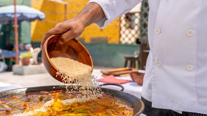 Chef adding rice to a delicious paella from a wooden bowl, cooking outdoors for a family lunch