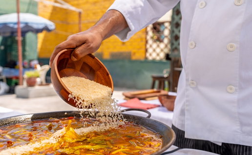 Chef adding rice to a delicious paella from a wooden bowl, cooking outdoors for a family lunch