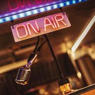 Glowing on air neon sign beside a vintage microphone in a cozy retro studio, evoking live radio