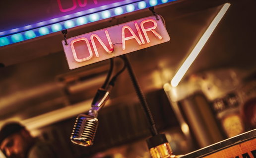 Glowing on air neon sign beside a vintage microphone in a cozy retro studio, evoking live radio
