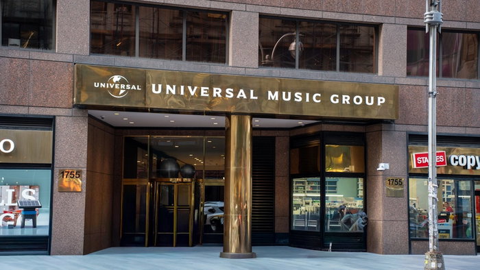 December 21 2025: Entrance of the Universal Music Group building on Broadway shows gold signage, glass doors, stone facade, street reflections in Midtown Manhattan