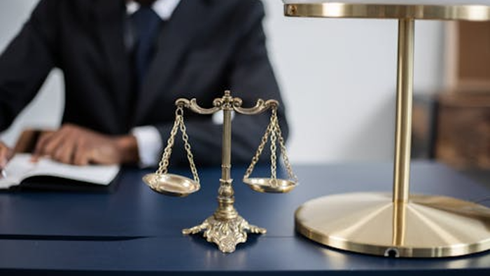 Lawyer sat at desk in background with brass balance scales and lamp on desl