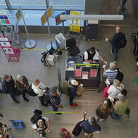 Passengers queue at an airport boarding gate while staff carry out cabin bag checks before departure.