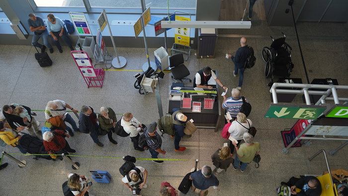 Passengers queue at an airport boarding gate while staff carry out cabin bag checks before departure.