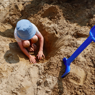 Child digging in the sand on the beach with a blue shovel stuck in the sand