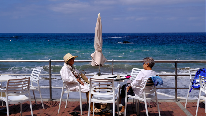 Two elderly women sitting at a table by the sea