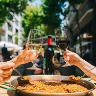 People sharing a large paella and wine at an outdoor restaurant in Spain as restaurants move towards smaller and more flexible portions under new food waste rules.