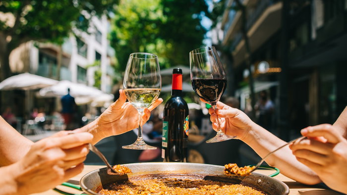 People sharing a large paella and wine at an outdoor restaurant in Spain as restaurants move towards smaller and more flexible portions under new food waste rules.