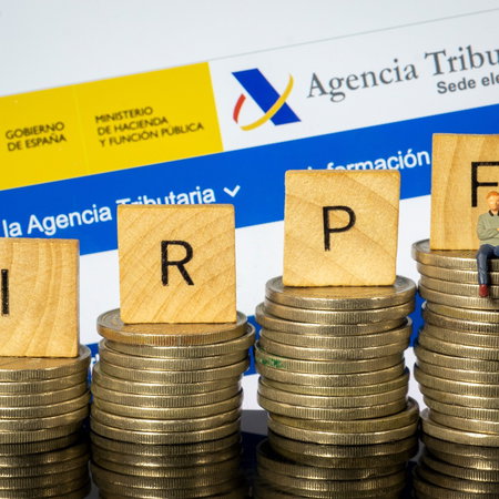 Spanish Tax Agency website displayed behind stacks of coins and IRPF tax blocks