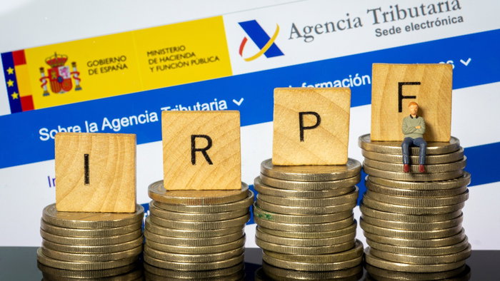 Spanish Tax Agency website displayed behind stacks of coins and IRPF tax blocks