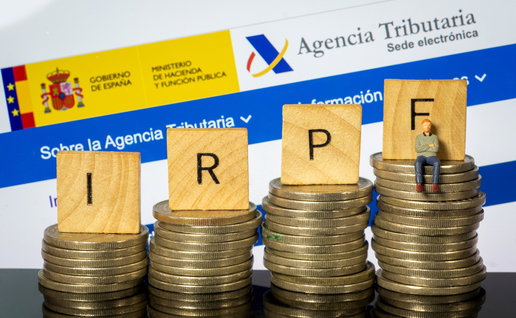 Spanish Tax Agency website displayed behind stacks of coins and IRPF tax blocks