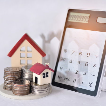 Calculator, coins and miniature houses symbolising rental deposits and housing costs in Spain.