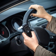A driver holding a portable alcohol breathalyser inside his car before starting the vehicle.