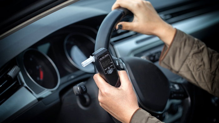 A driver holding a portable alcohol breathalyser inside his car before starting the vehicle.