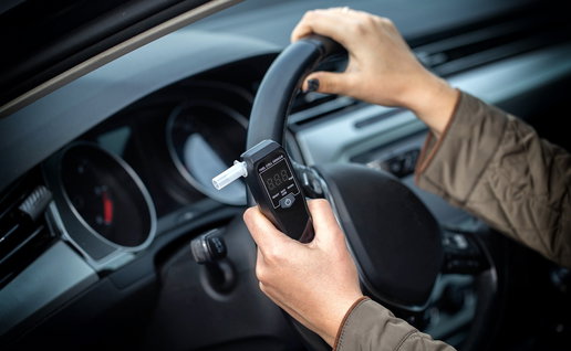 A driver holding a portable alcohol breathalyser inside his car before starting the vehicle.