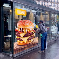 Large burger advertisement displayed on a fast food restaurant window in a European city
