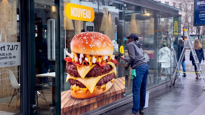 Large burger advertisement displayed on a fast food restaurant window in a European city