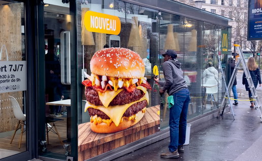 Large burger advertisement displayed on a fast food restaurant window in a European city