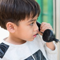 Young child using a public telephone to call home without a mobile phone.