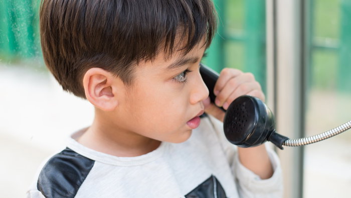 Young child using a public telephone to call home without a mobile phone.